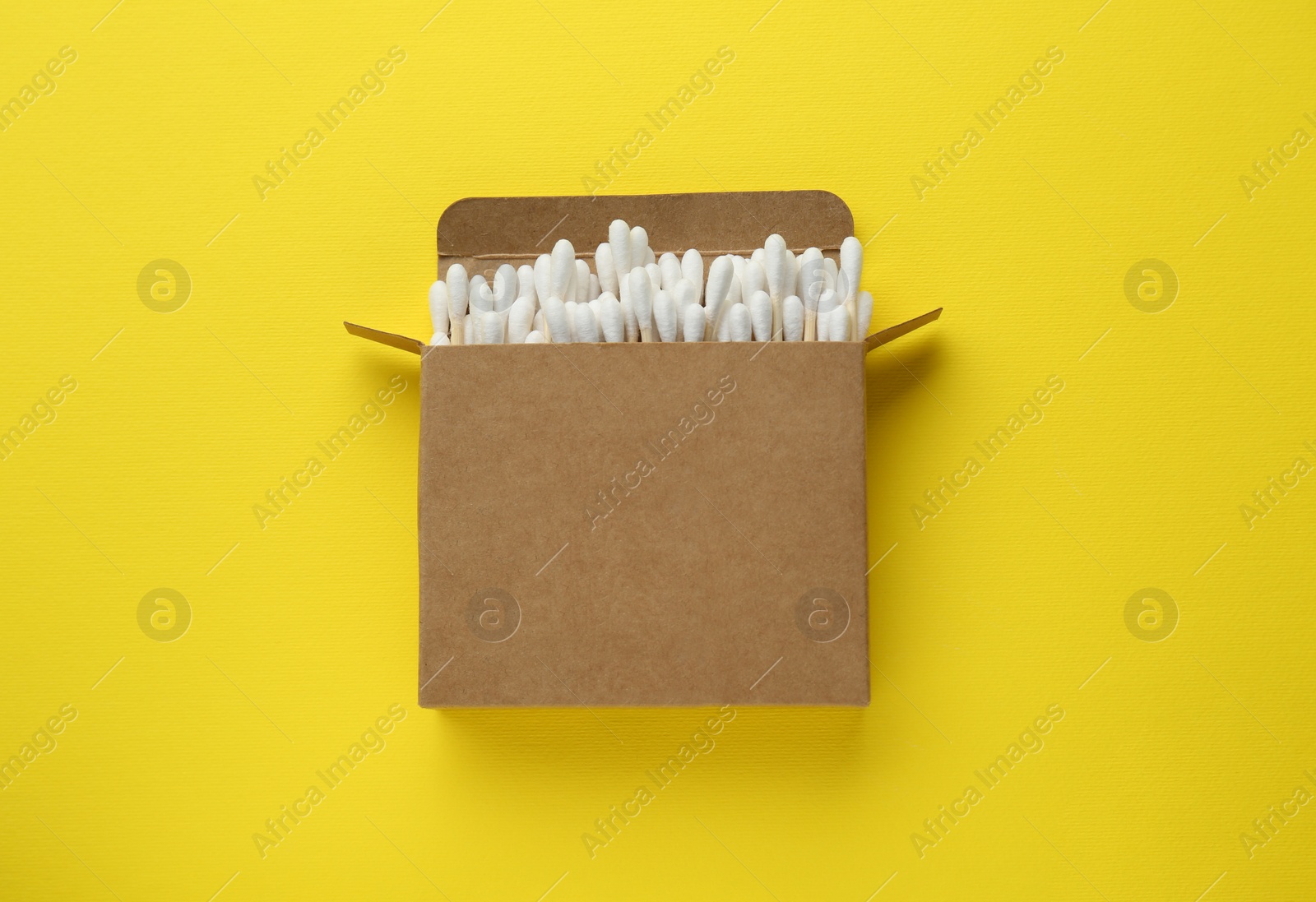 Photo of Cardboard box with cotton buds on yellow background, top view