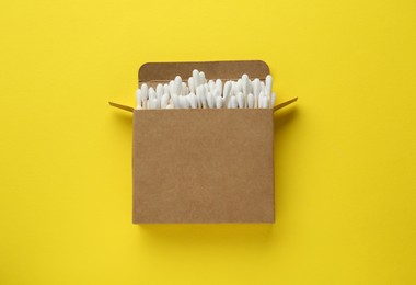 Photo of Cardboard box with cotton buds on yellow background, top view