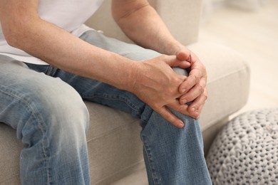 Senior man suffering from pain in leg indoors, closeup. Rheumatism symptom
