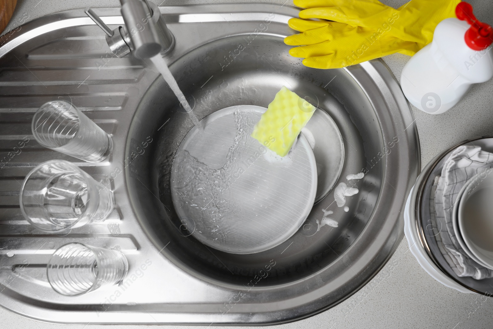 Photo of Washing plates, sponge and rubber gloves in kitchen sink, above view