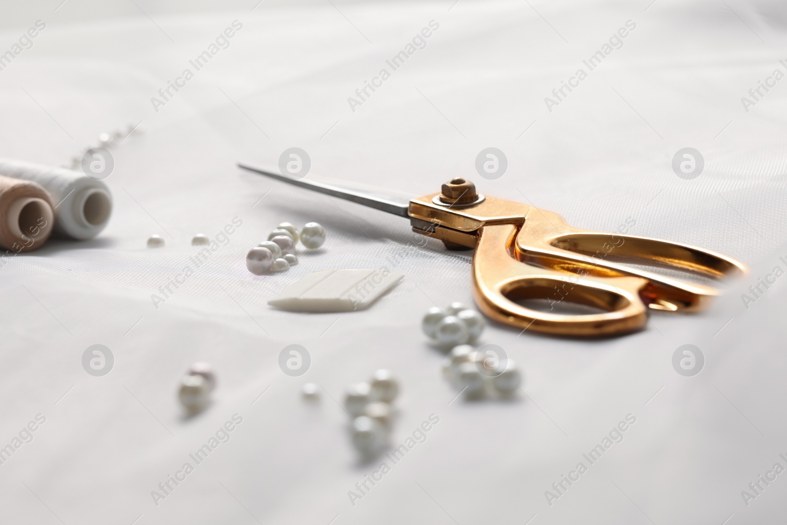 Photo of Pair of scissors, threads and beads on white fabric, closeup