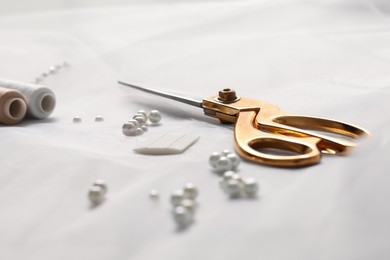 Photo of Pair of scissors, threads and beads on white fabric, closeup