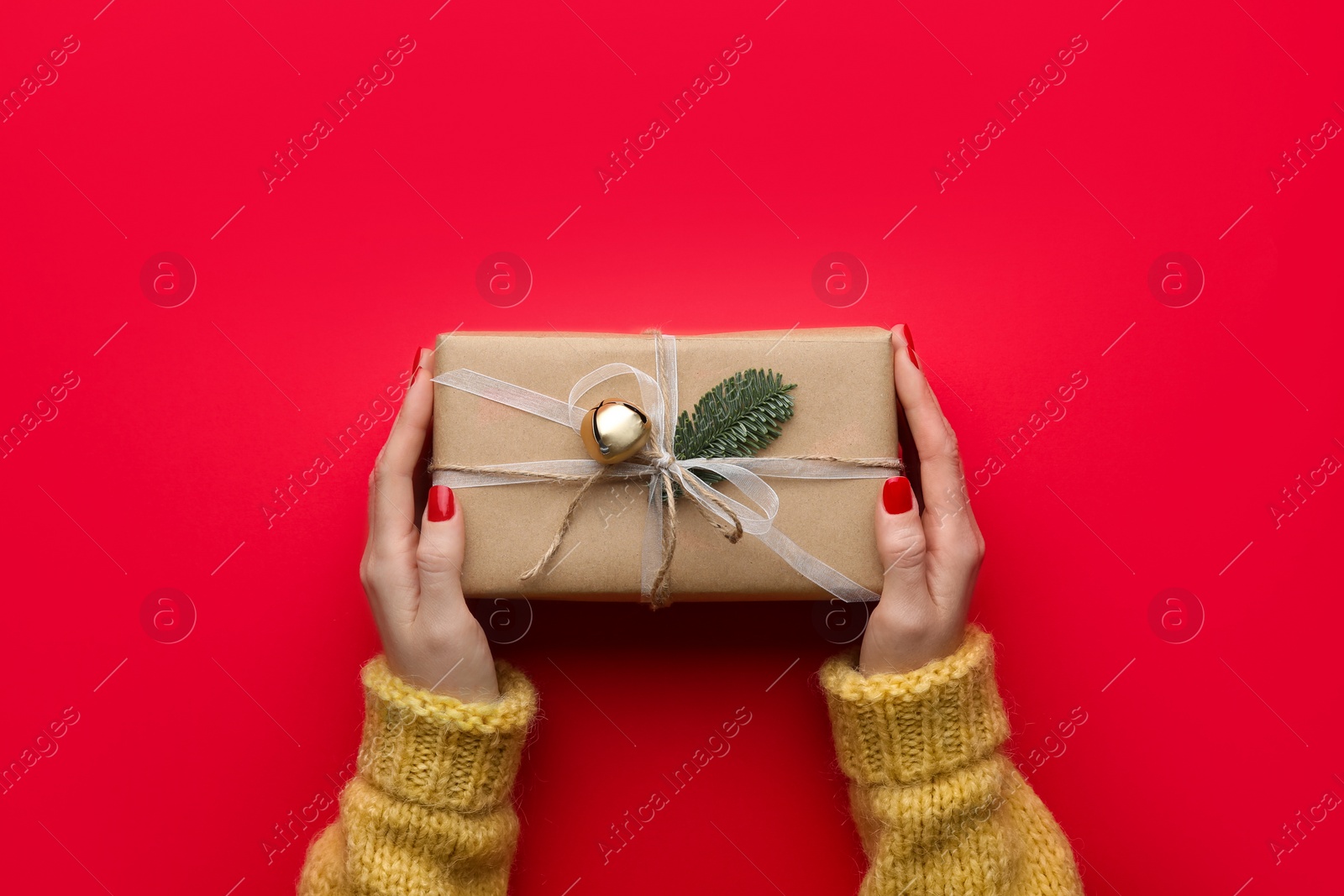 Photo of Woman holding Christmas gift box on red background, top view