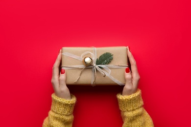 Woman holding Christmas gift box on red background, top view