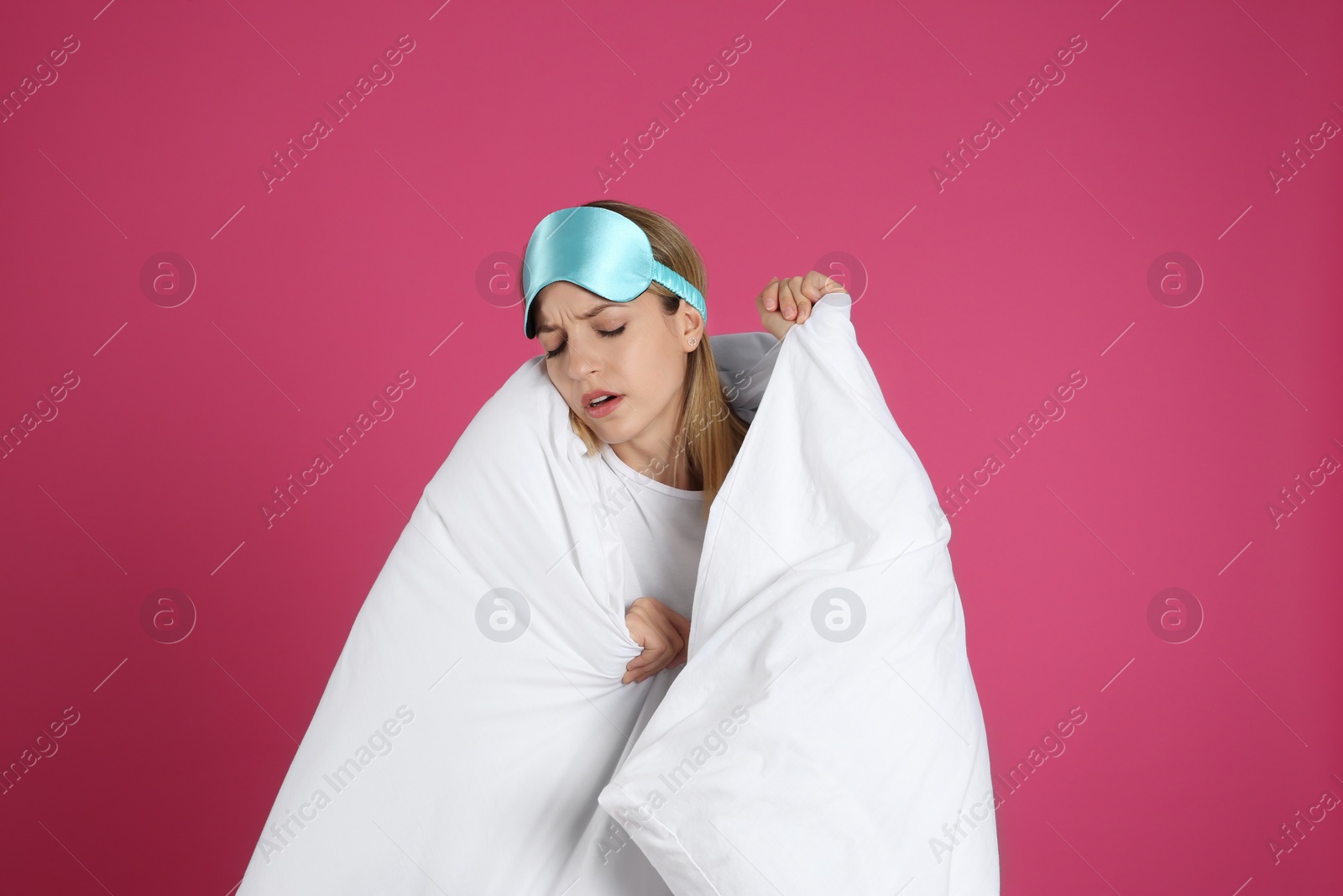 Photo of Young woman in sleeping mask wrapped with soft blanket on pink background