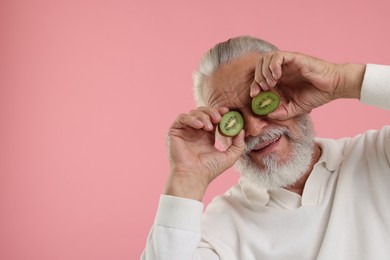 Photo of Senior man covering eyes with halves of kiwi on pink background, space for text