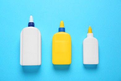 Photo of Different bottles of glues on light blue background, flat lay