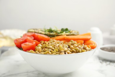 Delicious lentil bowl with avocado, tomatoes and carrots on white marble table