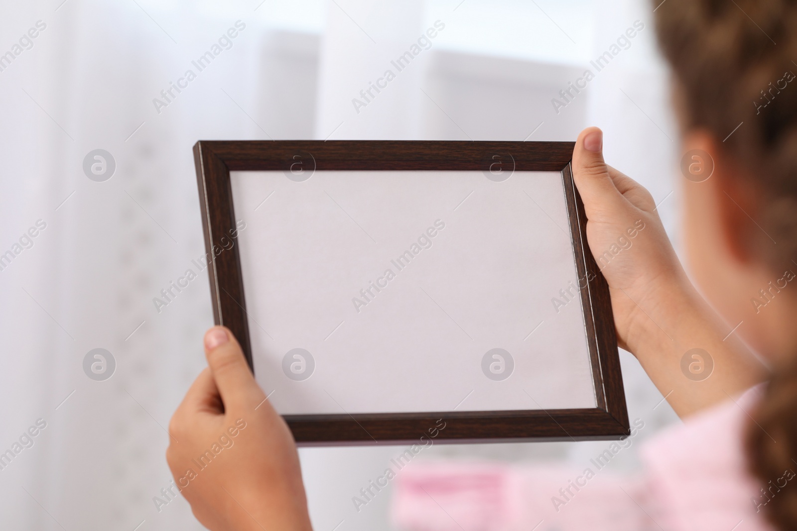 Photo of Little girl holding empty photo frame indoors, closeup