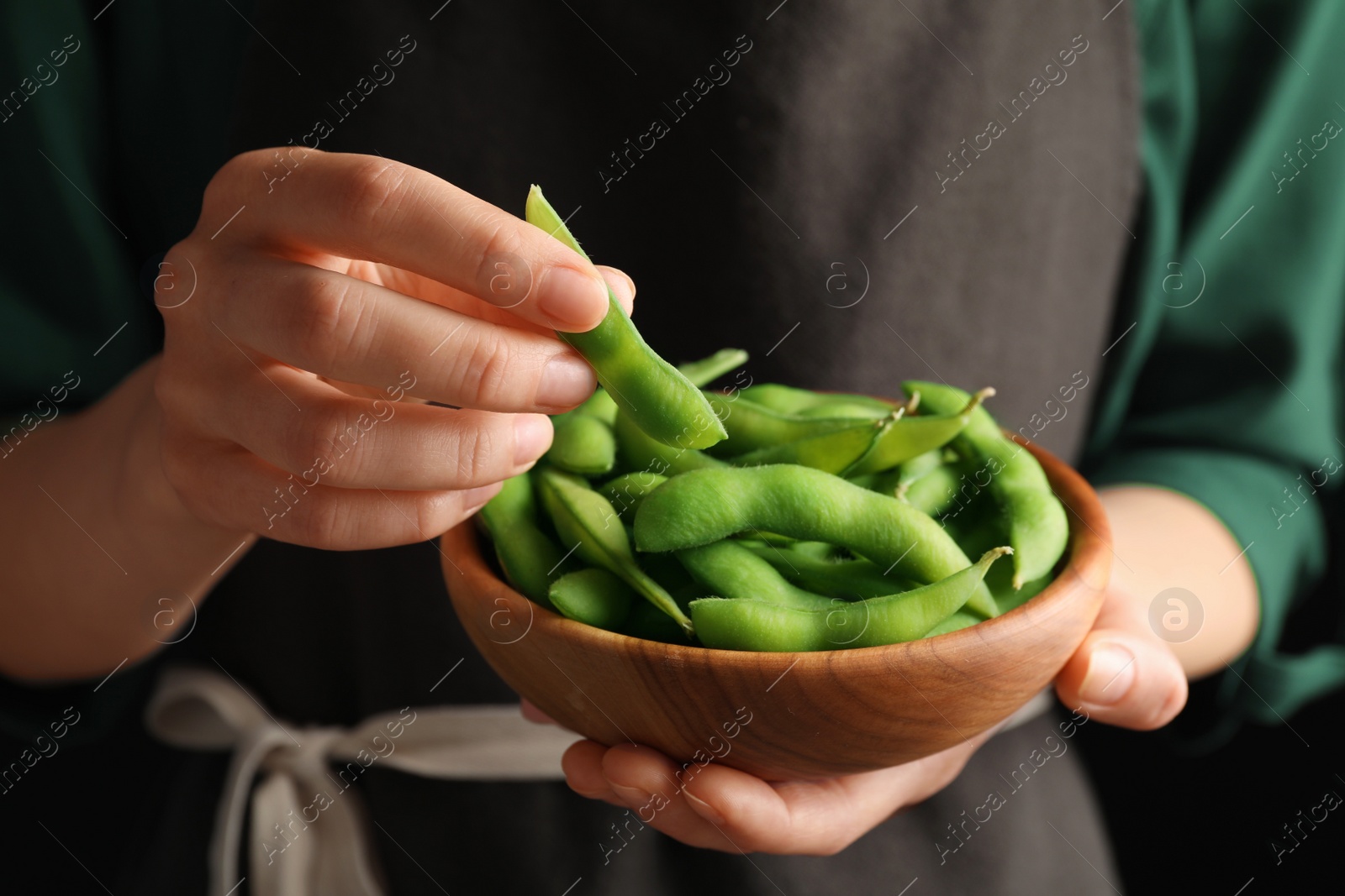 Photo of Woman holding bowl with green edamame beans in pods on black background, closeup