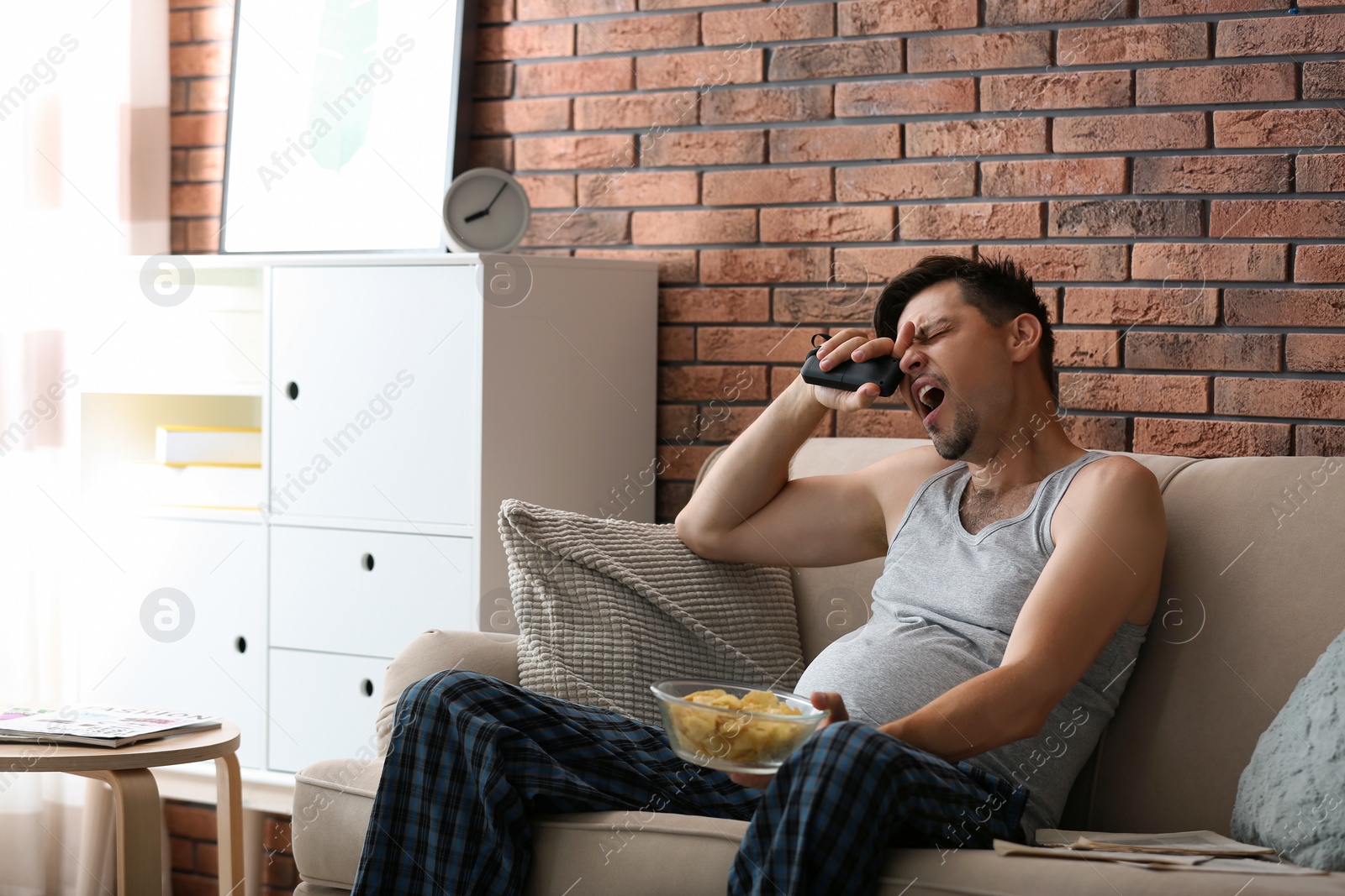 Photo of Lazy man with bowl of chips sitting on sofa at home