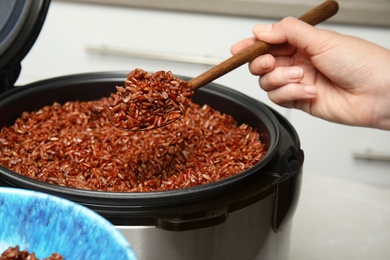 Woman putting delicious brown rice into bowl from multi cooker, closeup