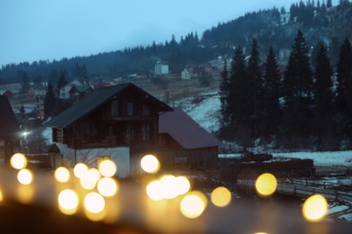 View of blurred Christmas lights and cottages near forest in winter evening