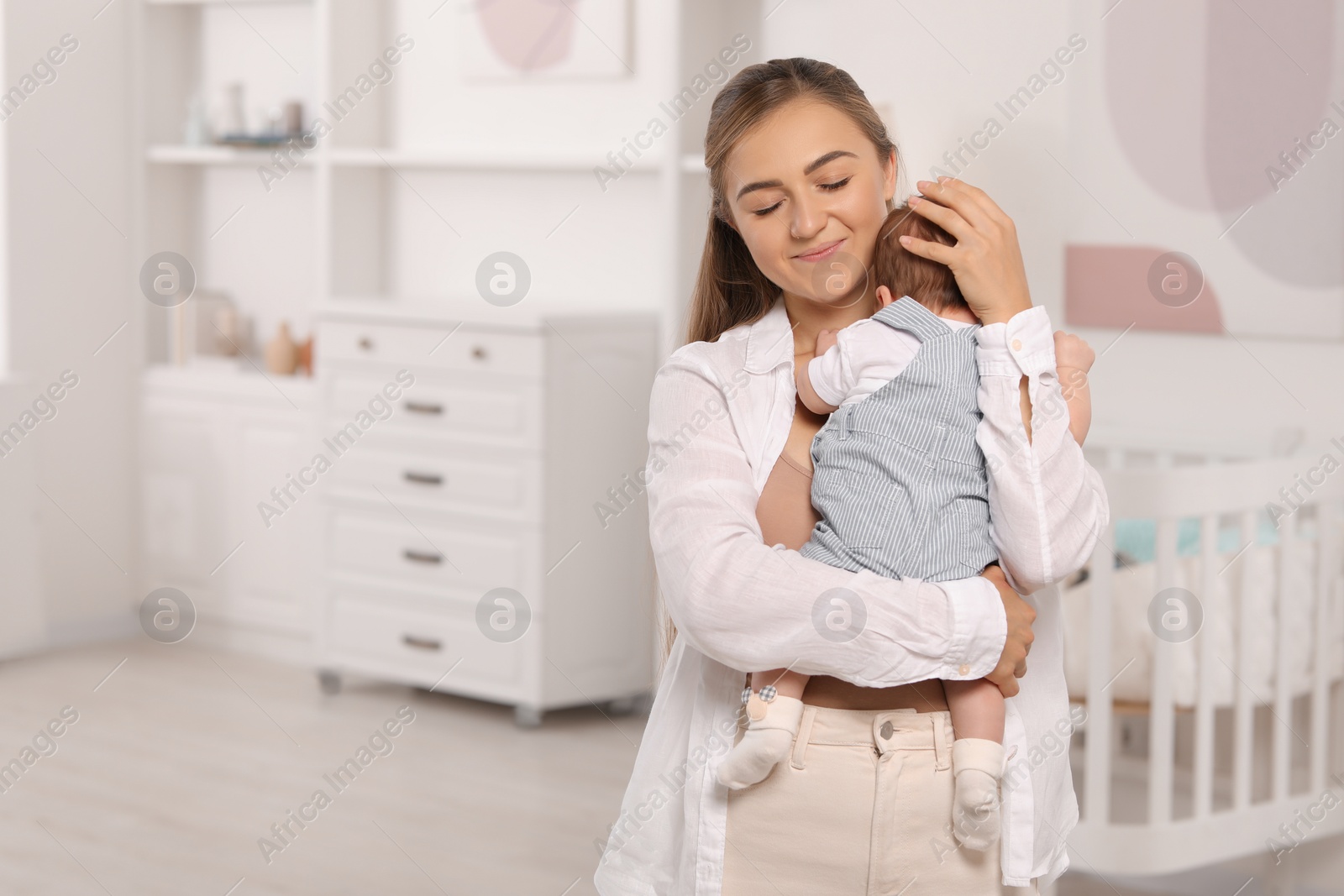 Photo of Mother holding her cute newborn baby in child's room, space for text