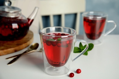 Photo of Tasty hot cranberry tea with mint and fresh berries on light table