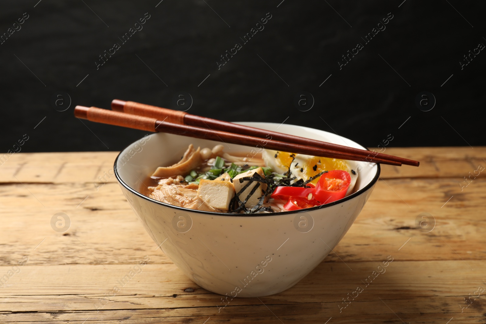 Photo of Bowl of delicious ramen and chopsticks on wooden table. Noodle soup