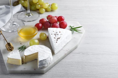 Photo of Tasty brie cheese with honey, rosemary and grapes on white wooden table, space for text