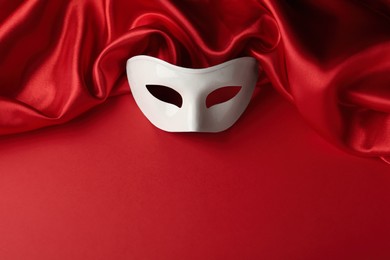 Photo of White theatre mask and fabric on red background, above view. Space for text