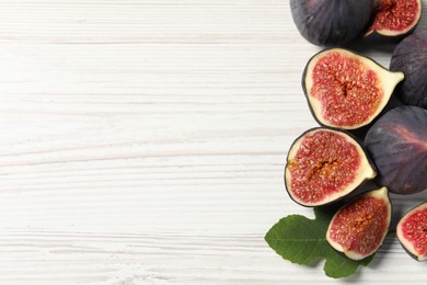 Photo of Whole and cut ripe figs on white wooden table, flat lay. Space for text