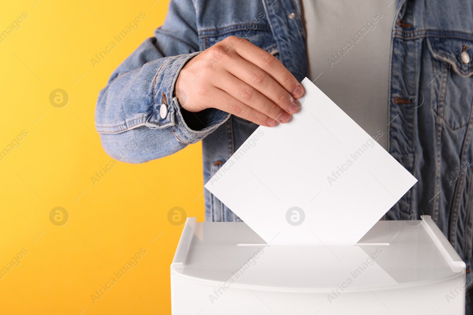 Photo of Man putting his vote into ballot box on yellow background, closeup