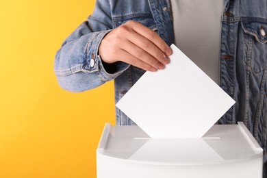 Man putting his vote into ballot box on yellow background, closeup