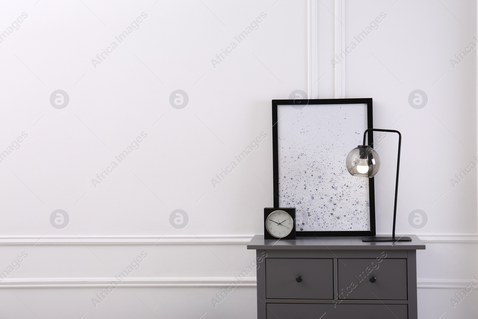 Photo of Grey wooden chest of drawers with lamp, clock and picture near white wall in room, space for text. Interior design