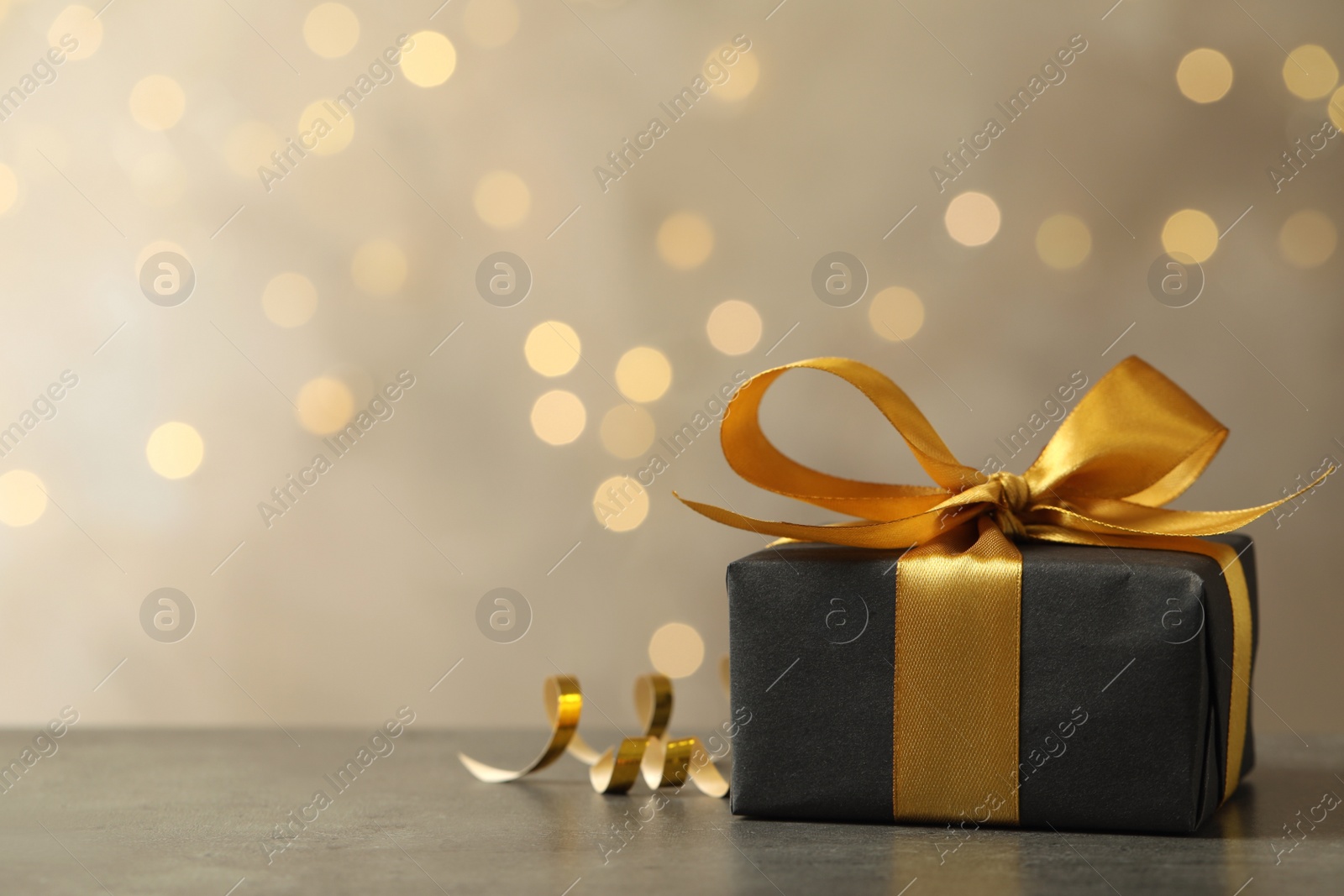 Photo of Beautifully wrapped gift box on grey table against blurred festive lights, space for text