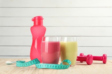 Photo of Tasty shakes, bottle, dumbbells, measuring tape and powder on wooden table. Weight loss