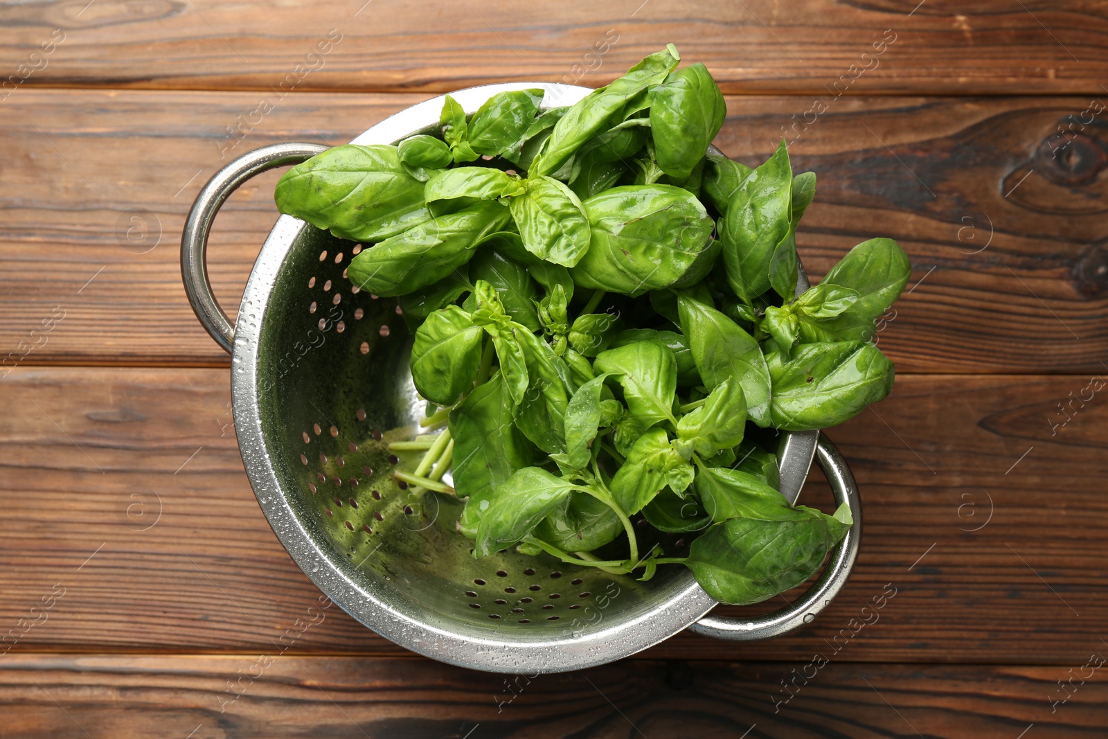 Photo of Metal colander with fresh basil leaves on wooden table, top view