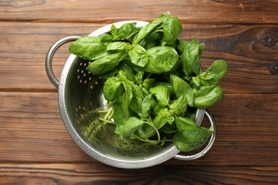 Metal colander with fresh basil leaves on wooden table, top view