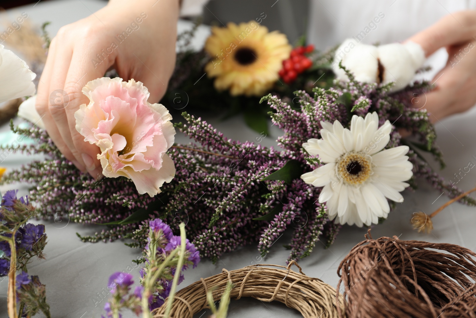 Photo of Florist making beautiful autumnal wreath with heather flowers at light grey table, closeup