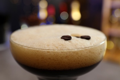 Photo of Glass of Espresso Martini with coffee beans on blurred background, closeup. Alcohol cocktail