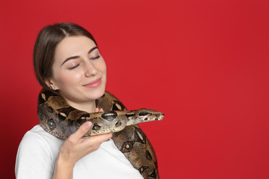Photo of Young woman with boa constrictor on red background, space for text. Exotic pet