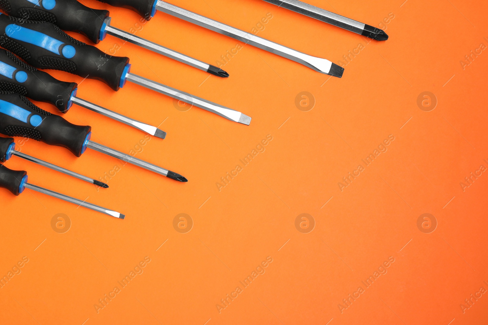 Photo of Set of screwdrivers on orange background, flat lay. Space for text
