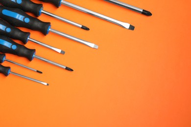 Set of screwdrivers on orange background, flat lay. Space for text