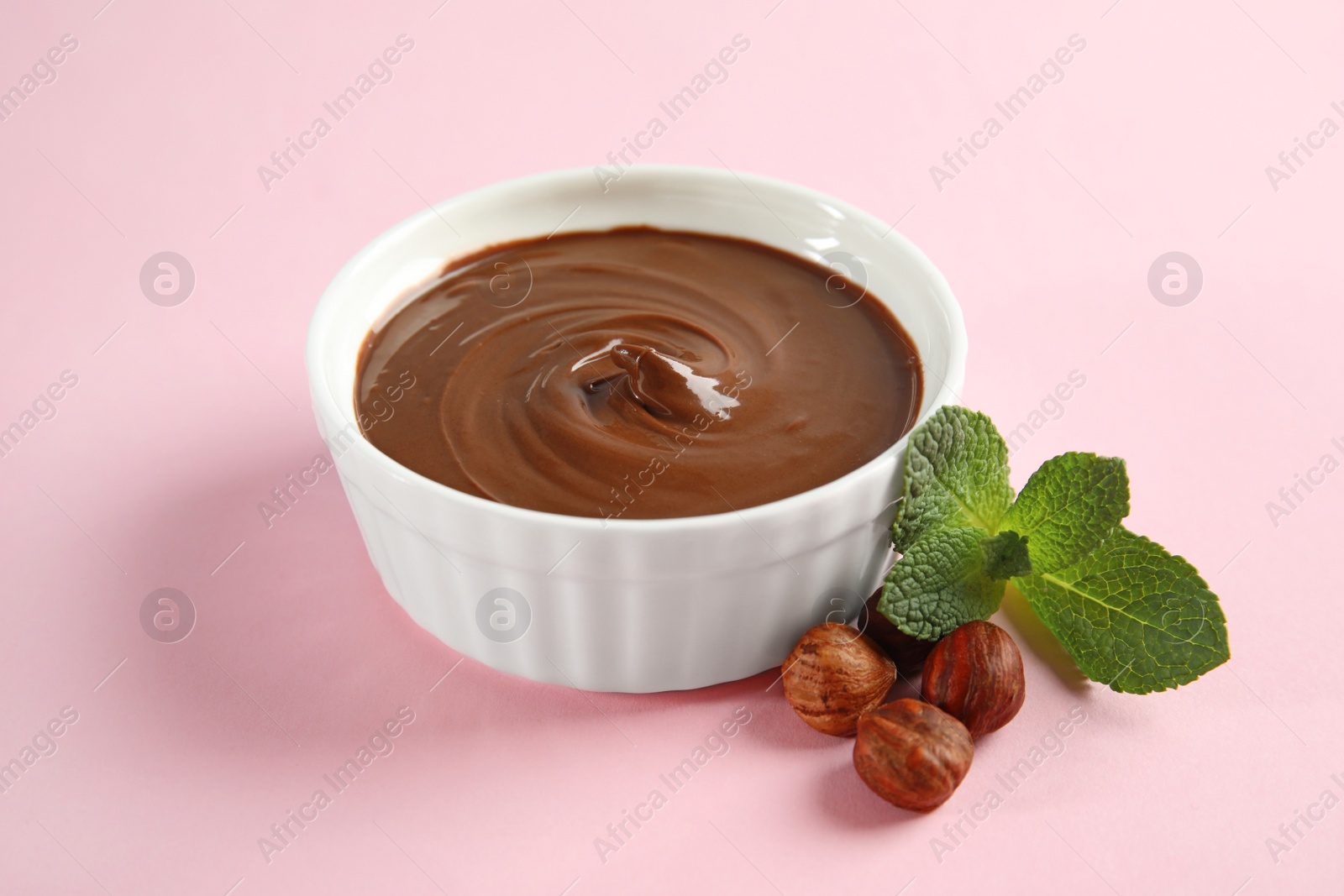 Photo of Dessert bowl with sweet chocolate cream, hazelnuts and mint on color background