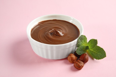 Photo of Dessert bowl with sweet chocolate cream, hazelnuts and mint on color background