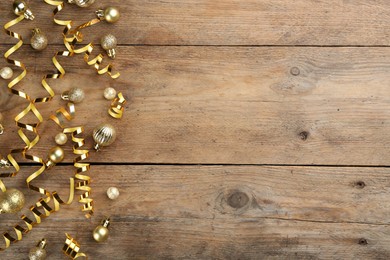 Shiny serpentine streamers and Christmas balls on wooden background, flat lay. Space for text