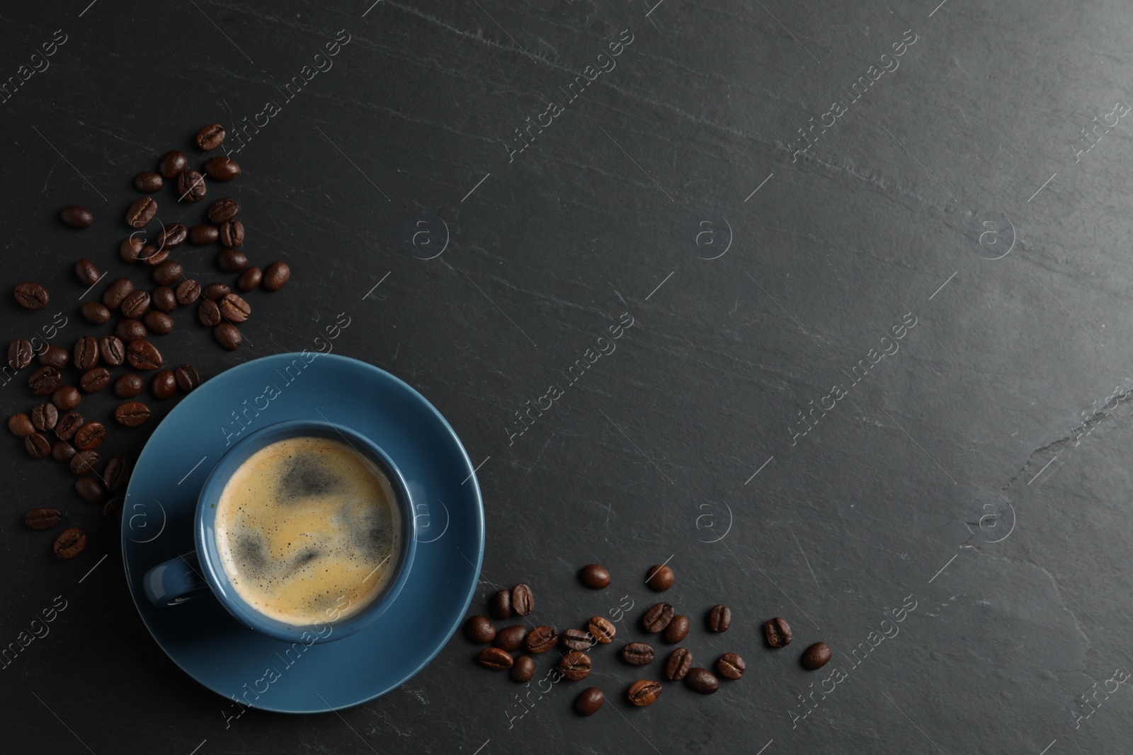 Photo of Cup of aromatic coffee and beans on black table, top view. Space for text