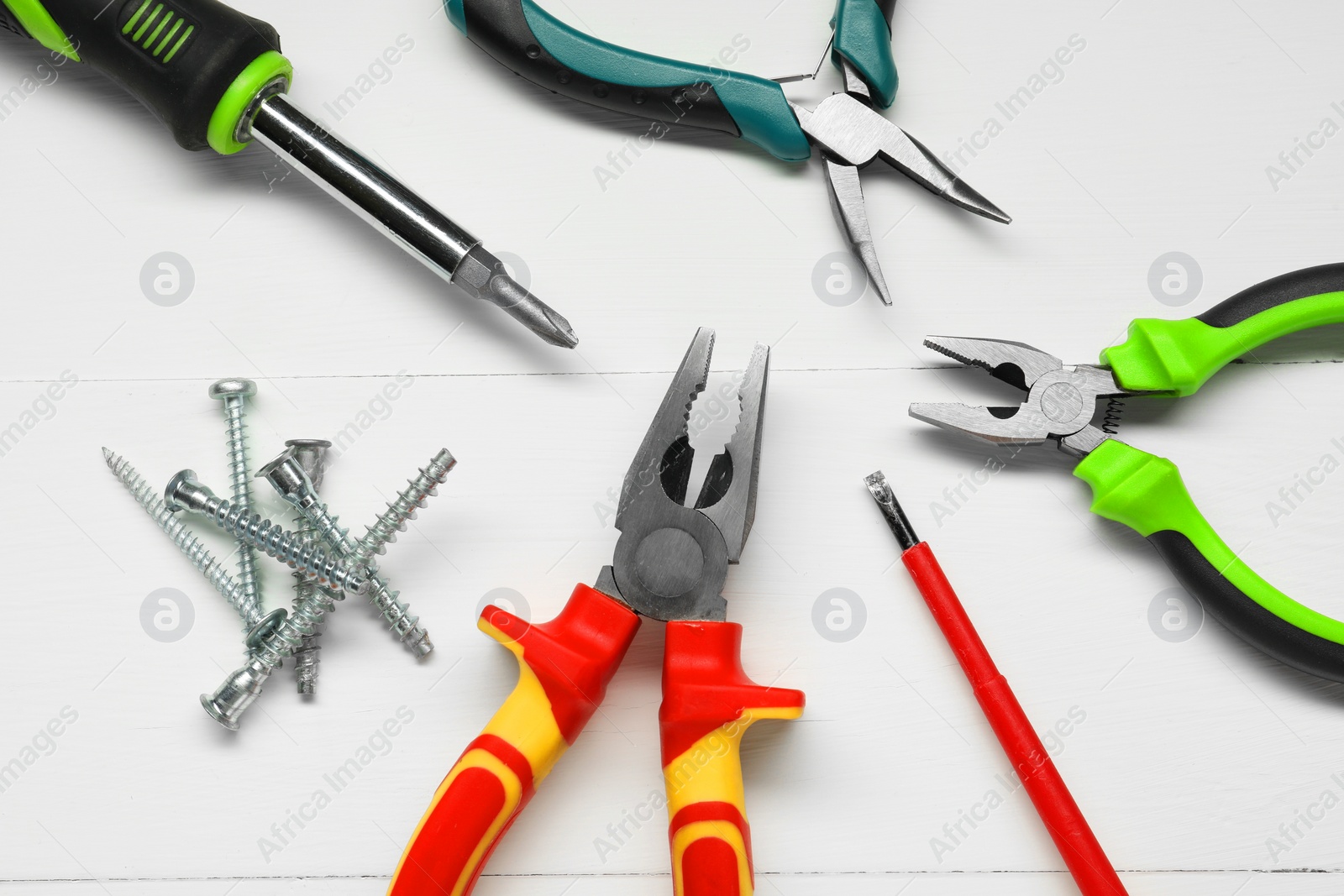 Photo of Pliers, screwdrivers and screws on white wooden table, flat lay