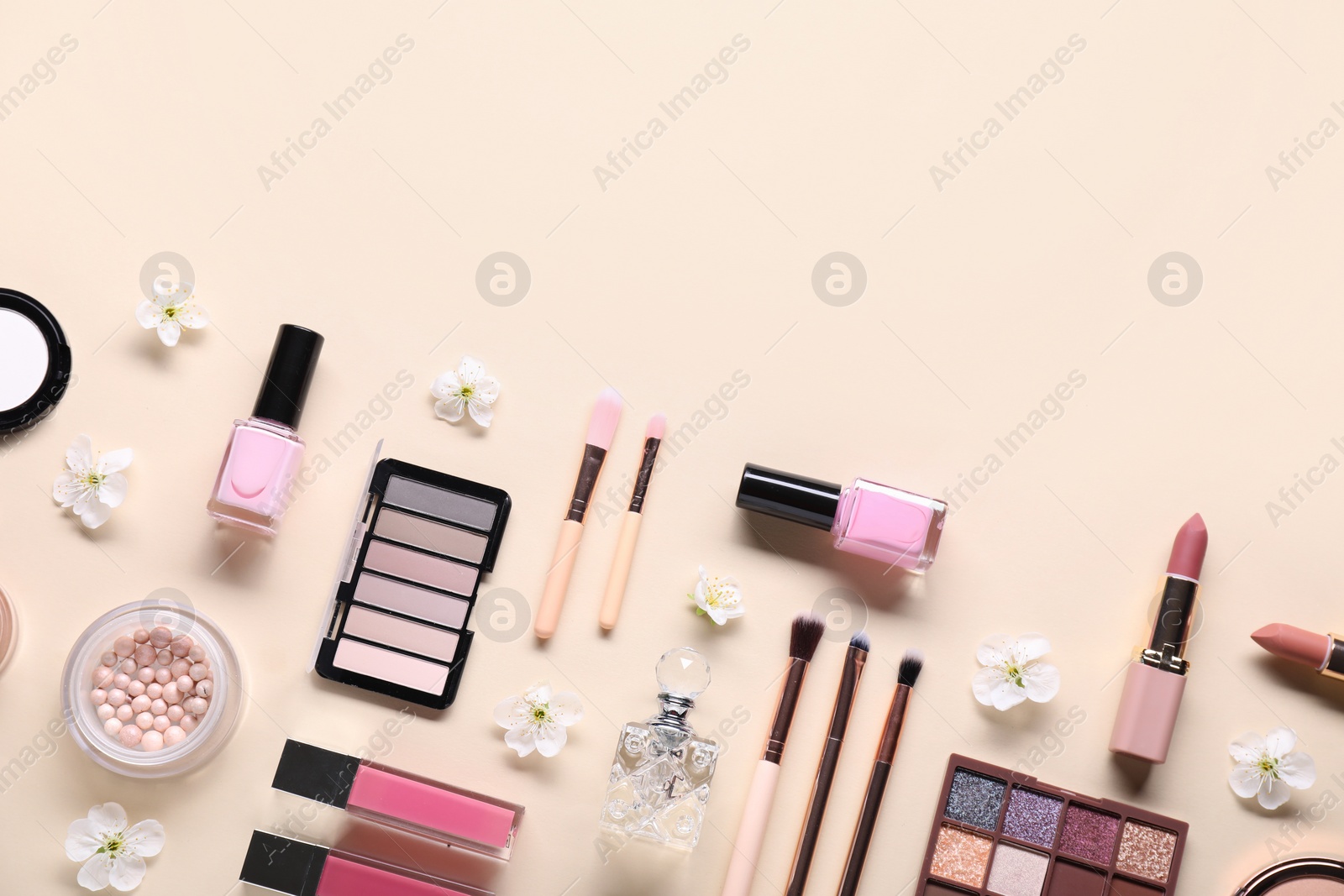 Photo of Flat lay composition with different makeup products and beautiful spring flowers on beige background, space for text