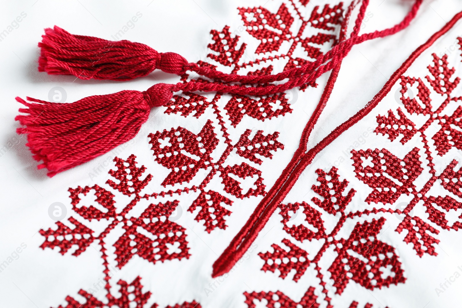 Photo of Beautiful red Ukrainian national embroidery on white fabric, closeup