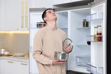 Upset man with pot near empty refrigerator in kitchen