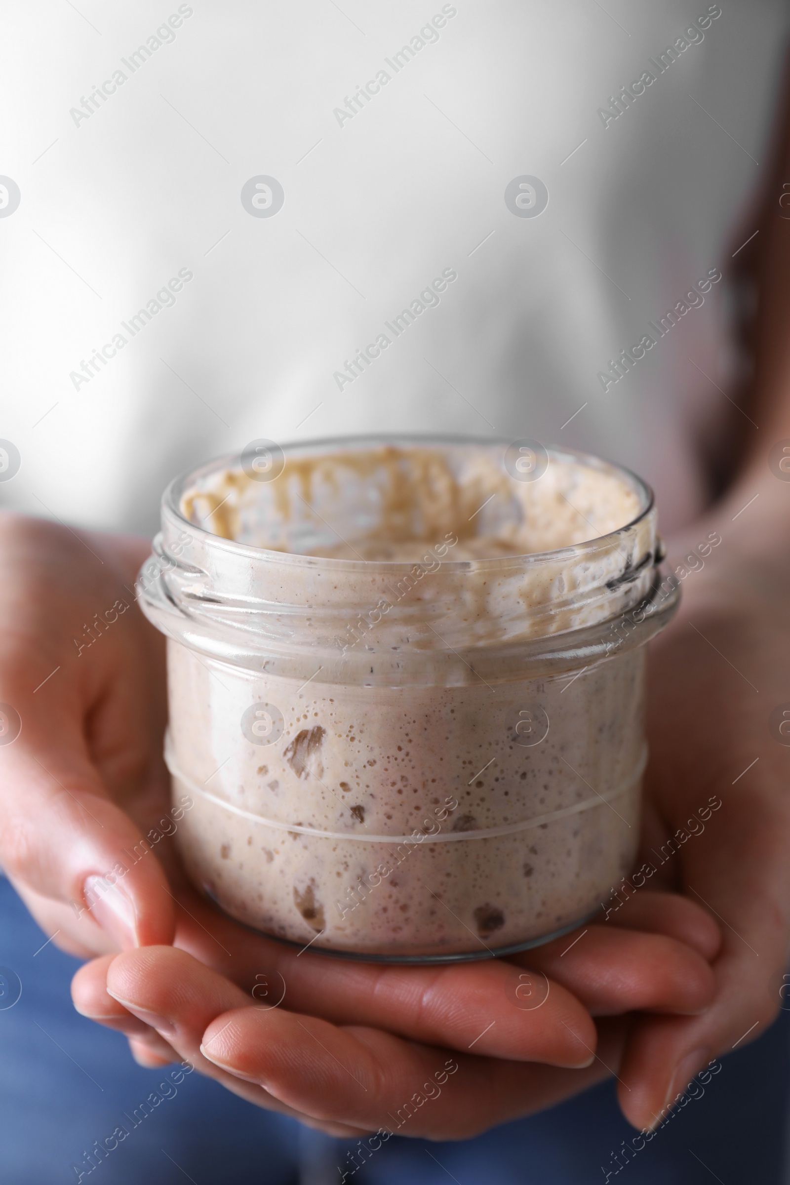 Photo of Woman holding glass jar with fresh sourdough starter, closeup