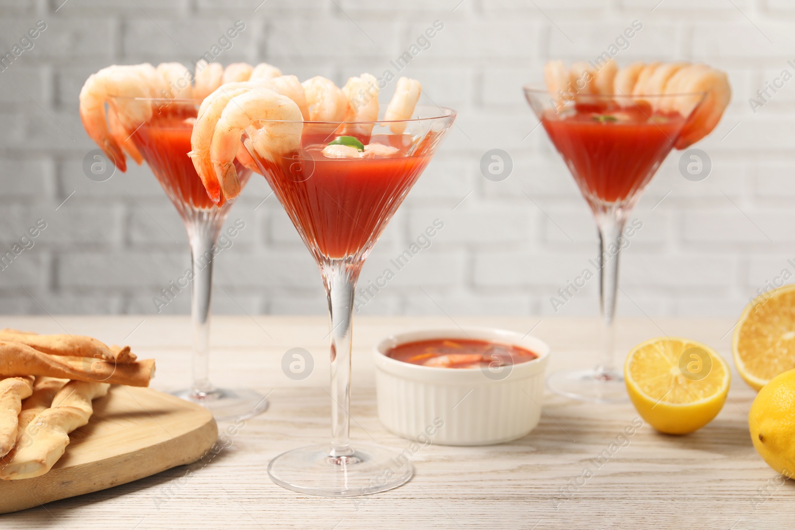 Photo of Tasty shrimp cocktail with sauce in glasses and lemon on light wooden table