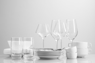 Photo of Set of many clean dishware, cutlery and glasses on light table