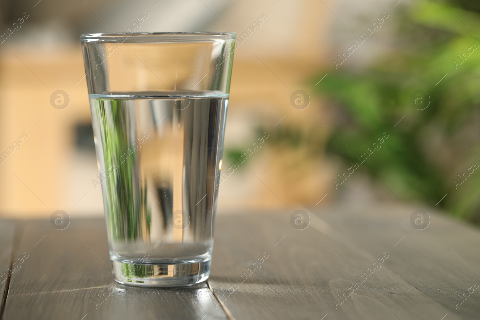 Photo of Glass of pure water on wooden table against blurred background, space for text