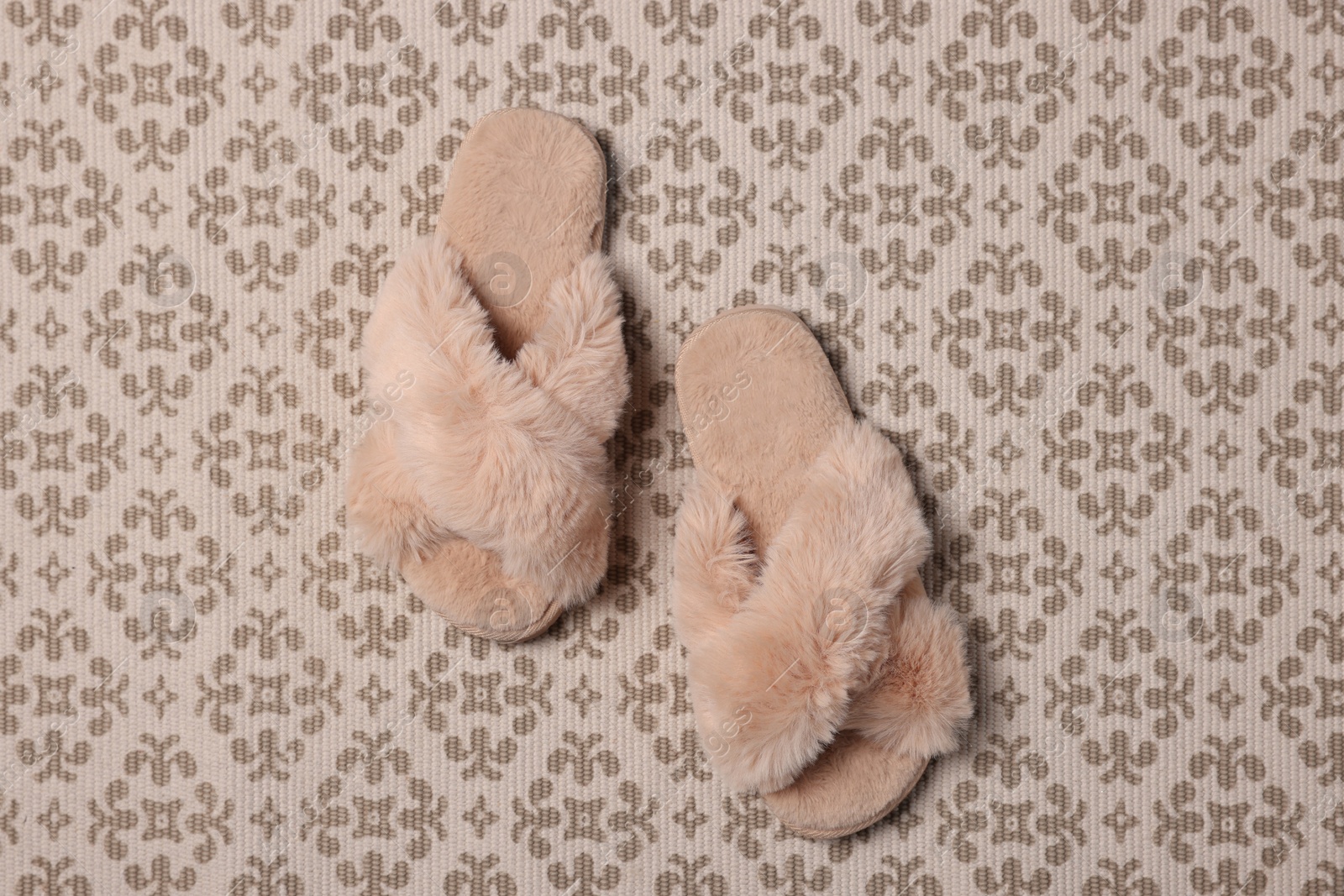 Photo of Fluffy beige slippers on carpet, top view