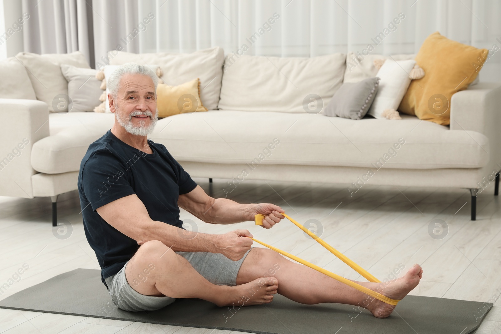 Photo of Senior man doing exercise with fitness elastic band on mat at home