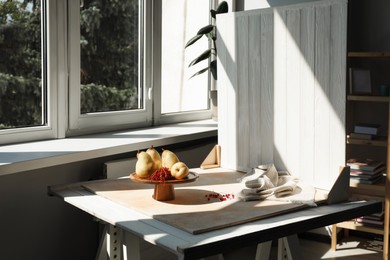 Photo of Stand with juicy pears, red currants and double-sided backdrop on table in photo studio